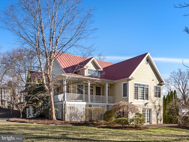 view of front facade featuring a standing seam roof, a front lawn, covered porch, and stone siding