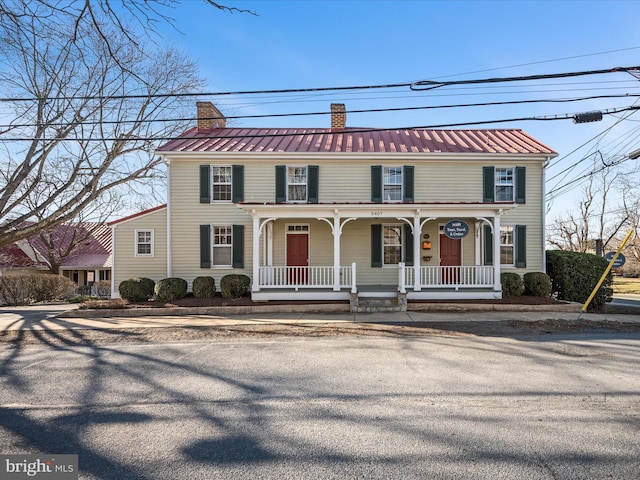 view of front of home with a porch, metal roof, and a chimney