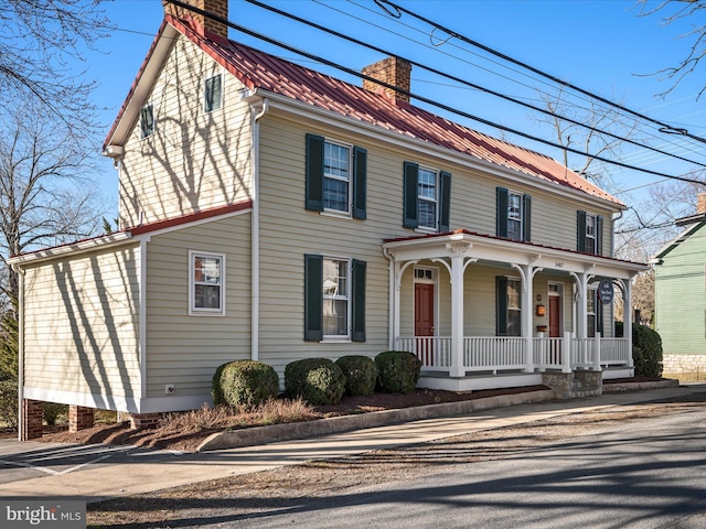 view of front facade with covered porch, a chimney, and metal roof