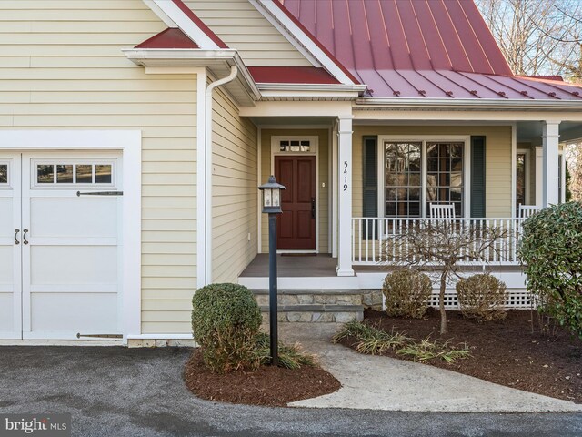 entrance to property featuring covered porch, an attached garage, metal roof, and a standing seam roof