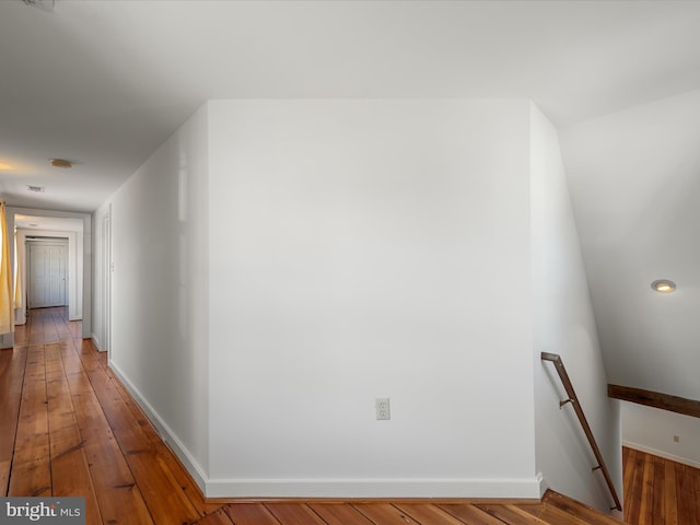 hall featuring an upstairs landing, baseboards, and wood-type flooring