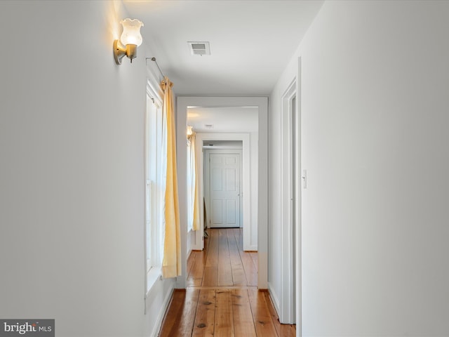 hall with visible vents, baseboards, and hardwood / wood-style floors