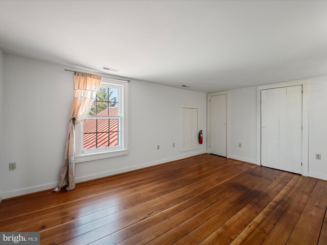 unfurnished bedroom featuring visible vents, multiple closets, baseboards, and wood-type flooring