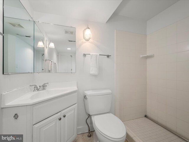 bathroom with a tile shower, visible vents, toilet, and vanity