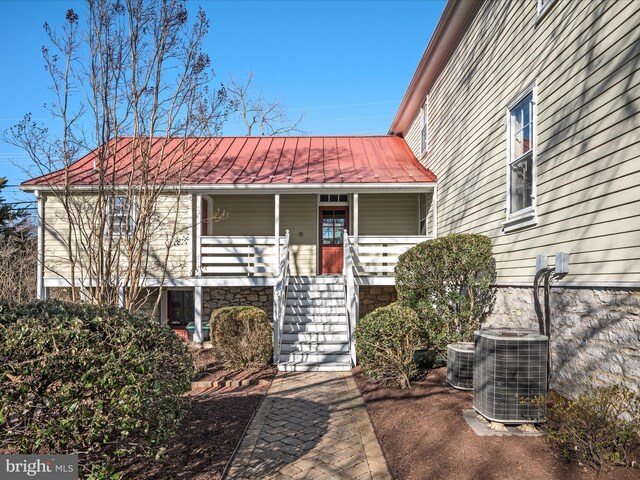 view of exterior entry with metal roof, central AC unit, a standing seam roof, and a porch