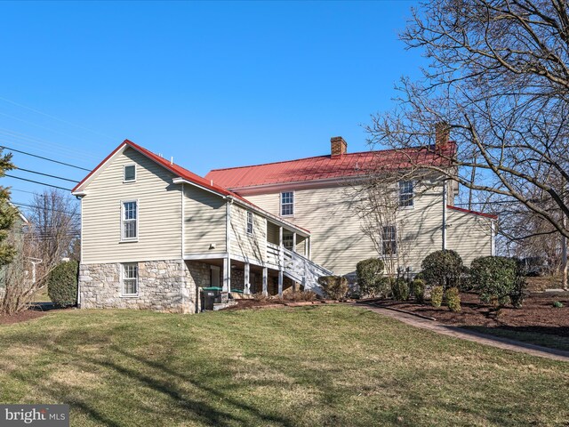 rear view of property with stairway, a lawn, a chimney, metal roof, and stone siding