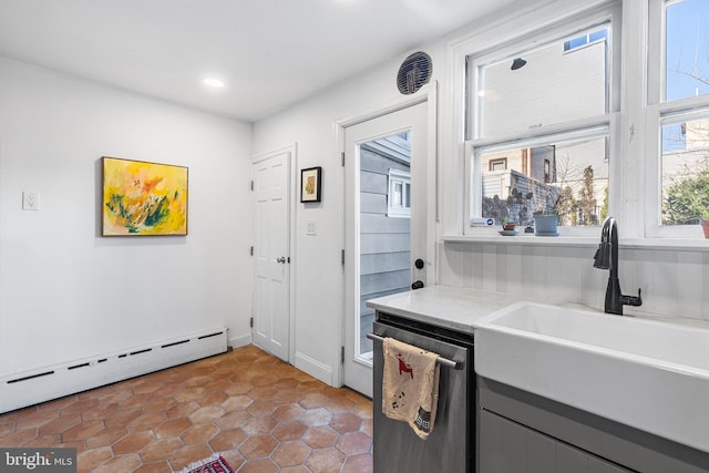 kitchen featuring light countertops, baseboard heating, gray cabinets, stainless steel dishwasher, and a sink