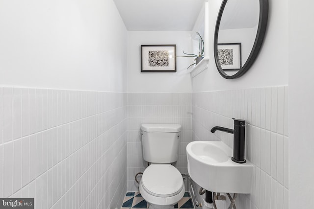 half bathroom with wainscoting, toilet, tile walls, and a sink