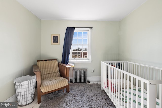 carpeted bedroom featuring baseboards, a crib, and radiator heating unit