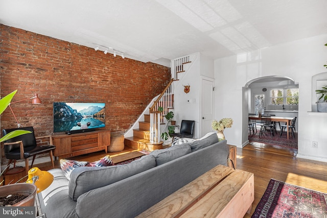 living room with track lighting, brick wall, stairway, wood finished floors, and arched walkways