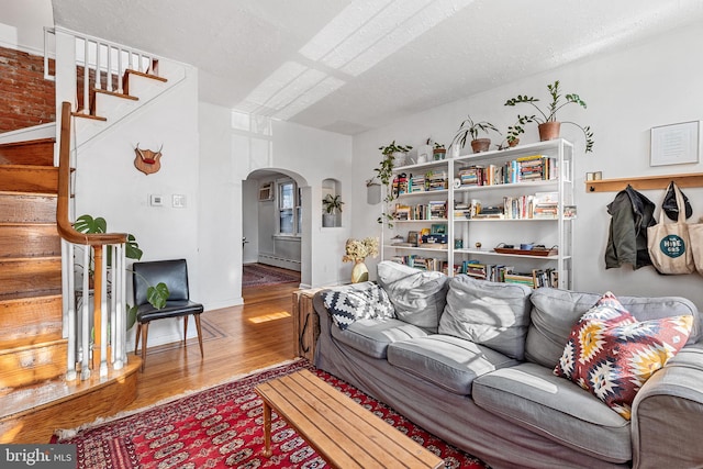 living room featuring wood finished floors, arched walkways, stairs, a textured ceiling, and baseboard heating