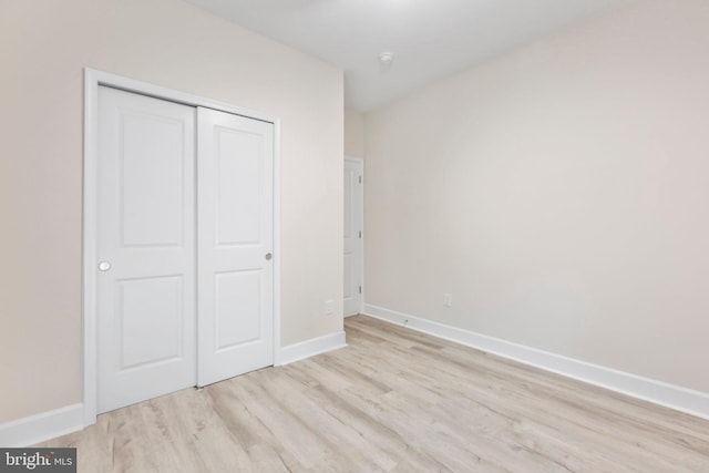 unfurnished bedroom featuring light wood-style flooring, baseboards, and a closet