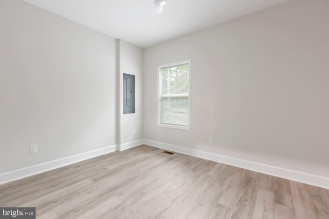 spare room with electric panel, light wood-type flooring, baseboards, and visible vents