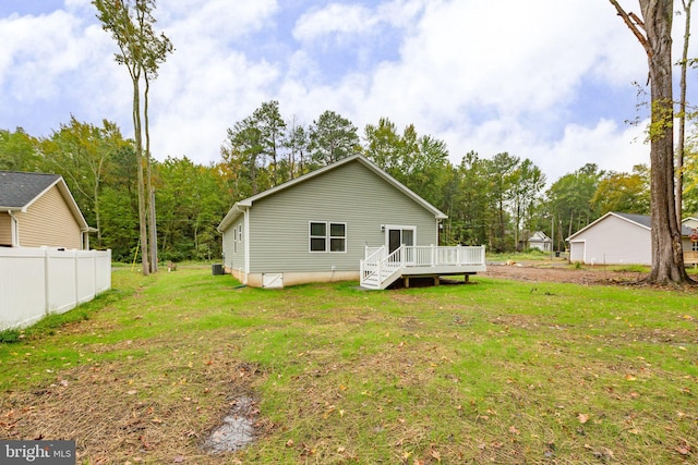 rear view of house featuring a wooden deck, a yard, and fence