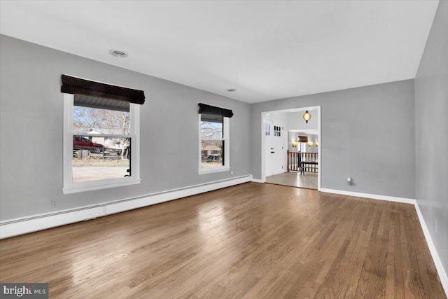 unfurnished living room featuring visible vents, wood finished floors, baseboards, and a baseboard radiator