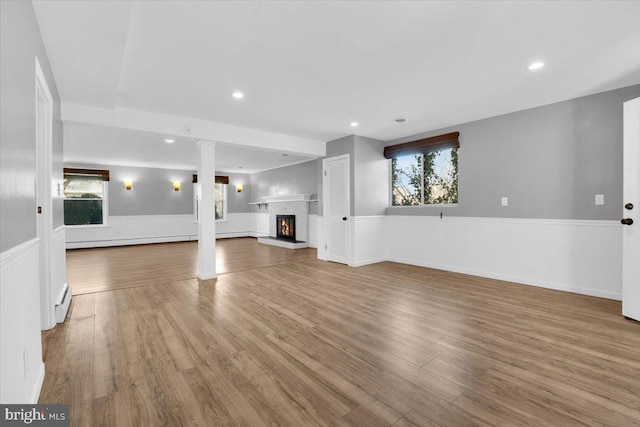 unfurnished living room with wood finished floors, recessed lighting, a fireplace, and a wainscoted wall