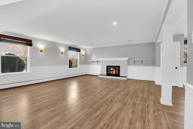 unfurnished living room featuring wood finished floors, wainscoting, a glass covered fireplace, crown molding, and baseboard heating