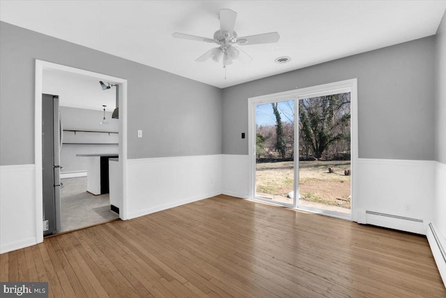 unfurnished room featuring visible vents, wainscoting, ceiling fan, and wood-type flooring