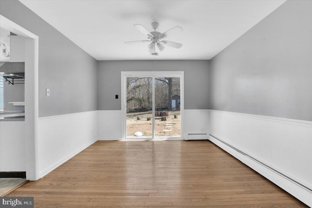 spare room featuring baseboard heating, wainscoting, a ceiling fan, and wood finished floors