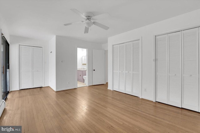 unfurnished bedroom featuring baseboards, two closets, ensuite bath, and light wood-style floors