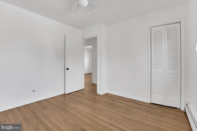 unfurnished bedroom featuring a ceiling fan, baseboards, light wood-style flooring, a closet, and baseboard heating