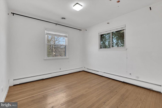 spare room featuring baseboard heating, plenty of natural light, visible vents, and wood-type flooring