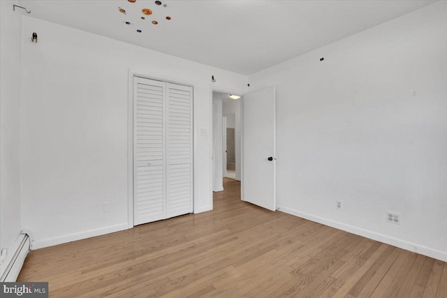 unfurnished bedroom with a closet, light wood-style floors, baseboards, and baseboard heating