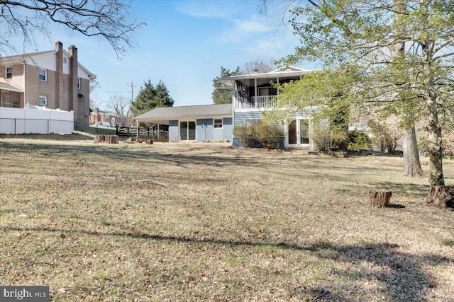 rear view of house with a lawn, a balcony, and fence