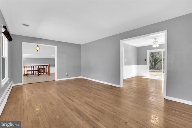 unfurnished living room with wood finished floors, baseboards, and a baseboard radiator