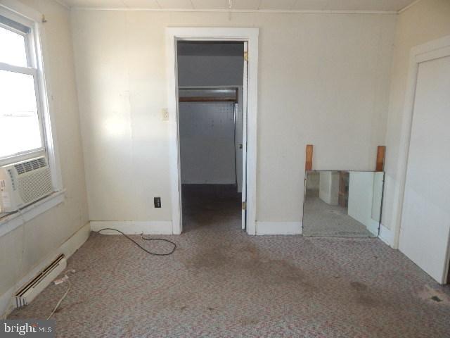 unfurnished bedroom with a walk in closet, carpet, baseboard heating, cooling unit, and a closet