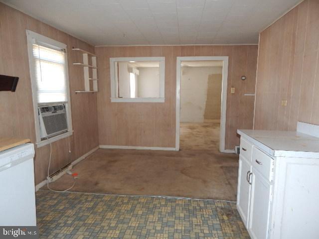 kitchen featuring wood walls, dishwasher, light countertops, cooling unit, and white cabinetry