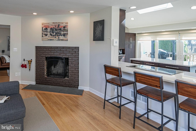 kitchen featuring light countertops, a kitchen bar, recessed lighting, a fireplace, and light wood-style floors