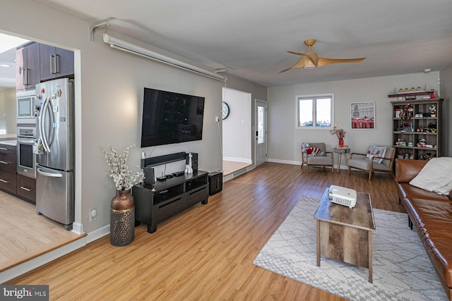 living room featuring light wood-style flooring, baseboards, and a ceiling fan