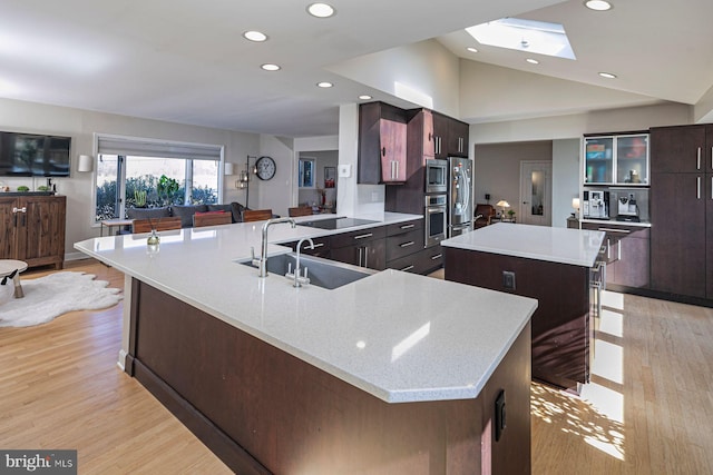 kitchen with lofted ceiling with skylight, light wood-style flooring, a sink, a spacious island, and appliances with stainless steel finishes