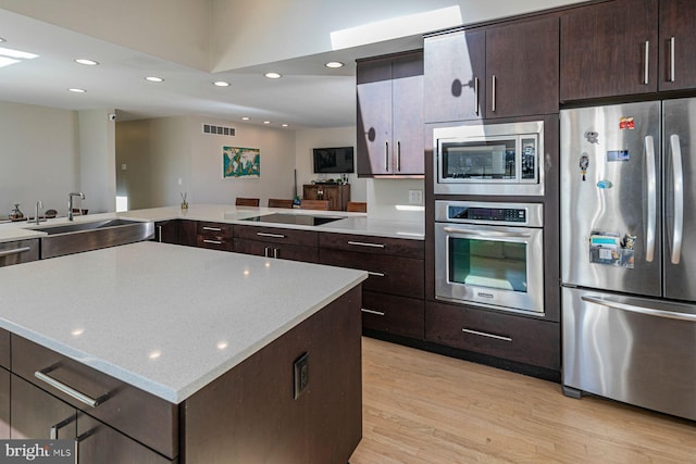 kitchen featuring dark brown cabinets, light wood-style floors, appliances with stainless steel finishes, and a sink