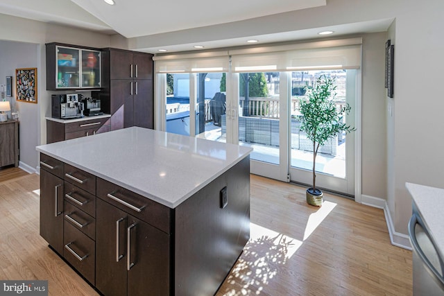 kitchen featuring dark brown cabinets, a kitchen island, glass insert cabinets, baseboards, and light wood-style flooring