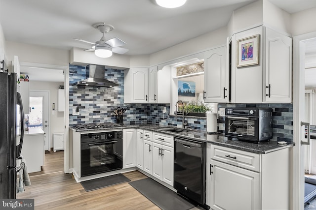 kitchen with a sink, black appliances, white cabinets, and wall chimney range hood