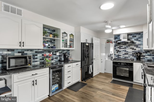 kitchen featuring visible vents, wall chimney range hood, wine cooler, white cabinets, and black appliances