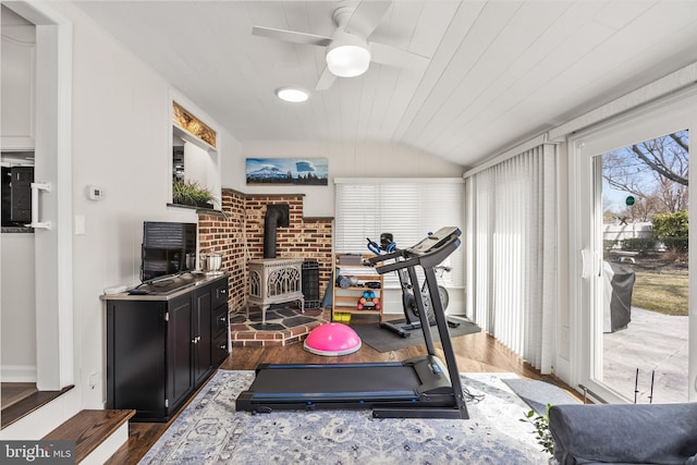 exercise area with vaulted ceiling, wooden ceiling, a wood stove, wood finished floors, and a ceiling fan