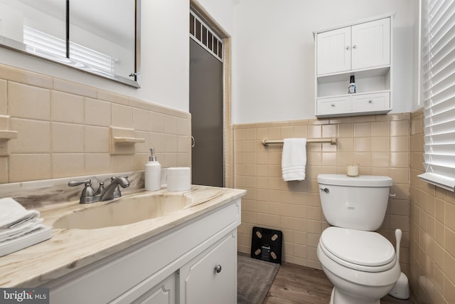 bathroom featuring toilet, wood finished floors, tile walls, wainscoting, and vanity