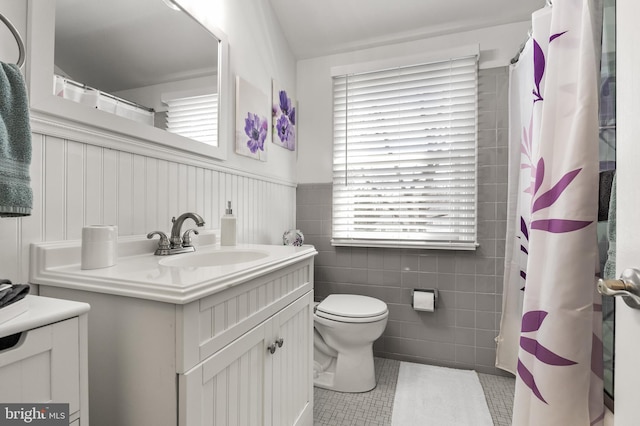 bathroom with tile walls, toilet, wainscoting, tile patterned floors, and vanity