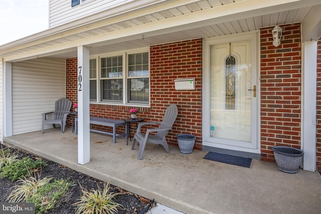 view of exterior entry featuring brick siding and a porch