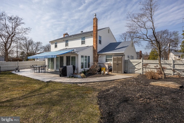 rear view of house with a chimney, a yard, a fenced backyard, a patio area, and a gate