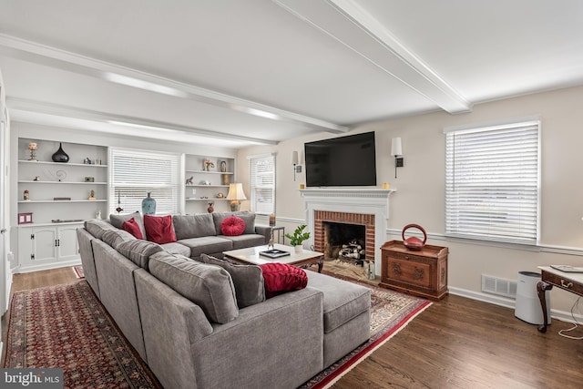 living area featuring visible vents, beam ceiling, wood finished floors, baseboards, and a brick fireplace