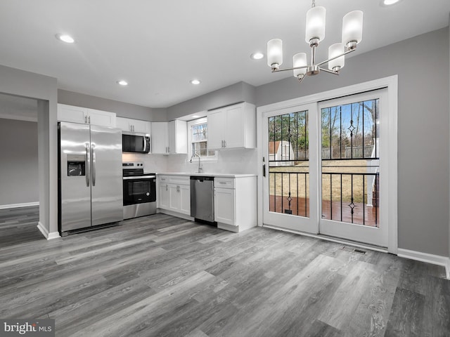 kitchen featuring wood finished floors, recessed lighting, a sink, white cabinets, and appliances with stainless steel finishes