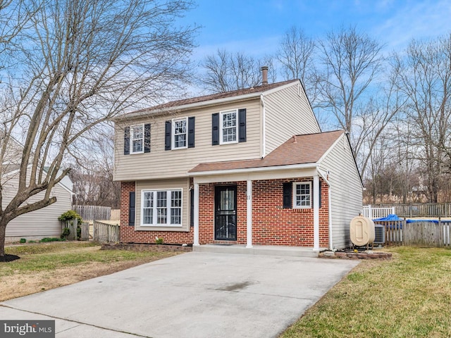 colonial home with brick siding, a shingled roof, a front lawn, fence, and a swimming pool