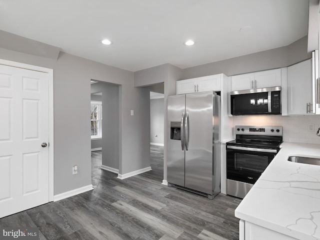 kitchen featuring backsplash, light stone counters, stainless steel appliances, dark wood-style floors, and white cabinetry