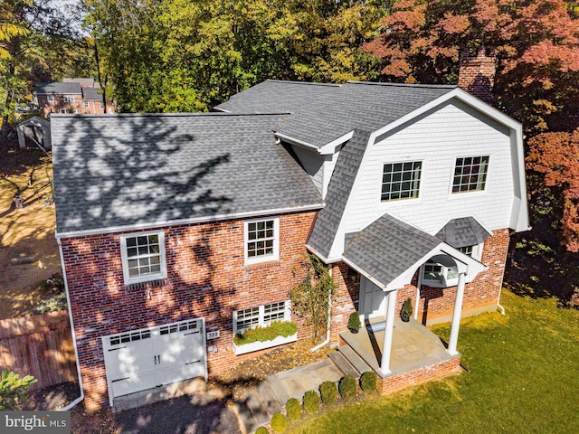 view of front of property featuring brick siding, a front lawn, roof with shingles, a chimney, and an attached garage