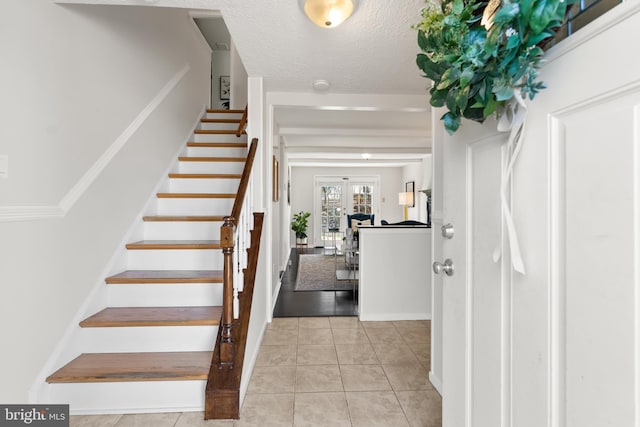 foyer entrance featuring a textured ceiling, light tile patterned flooring, and stairs