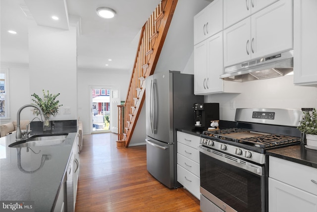 kitchen with under cabinet range hood, a sink, wood finished floors, stainless steel appliances, and white cabinets